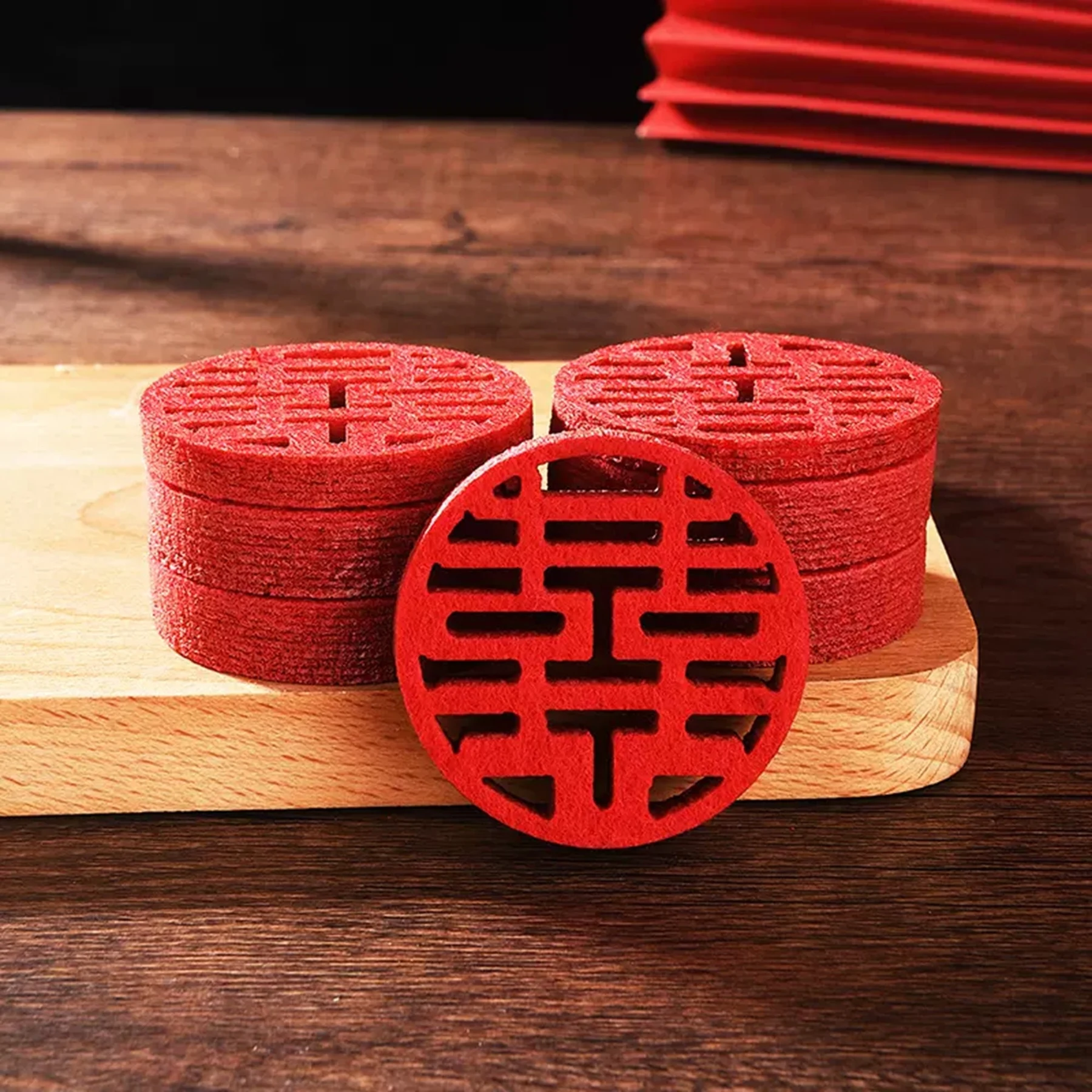 May include: A stack of red felt coasters with a double happiness symbol cut out. The coasters are on a wooden surface.