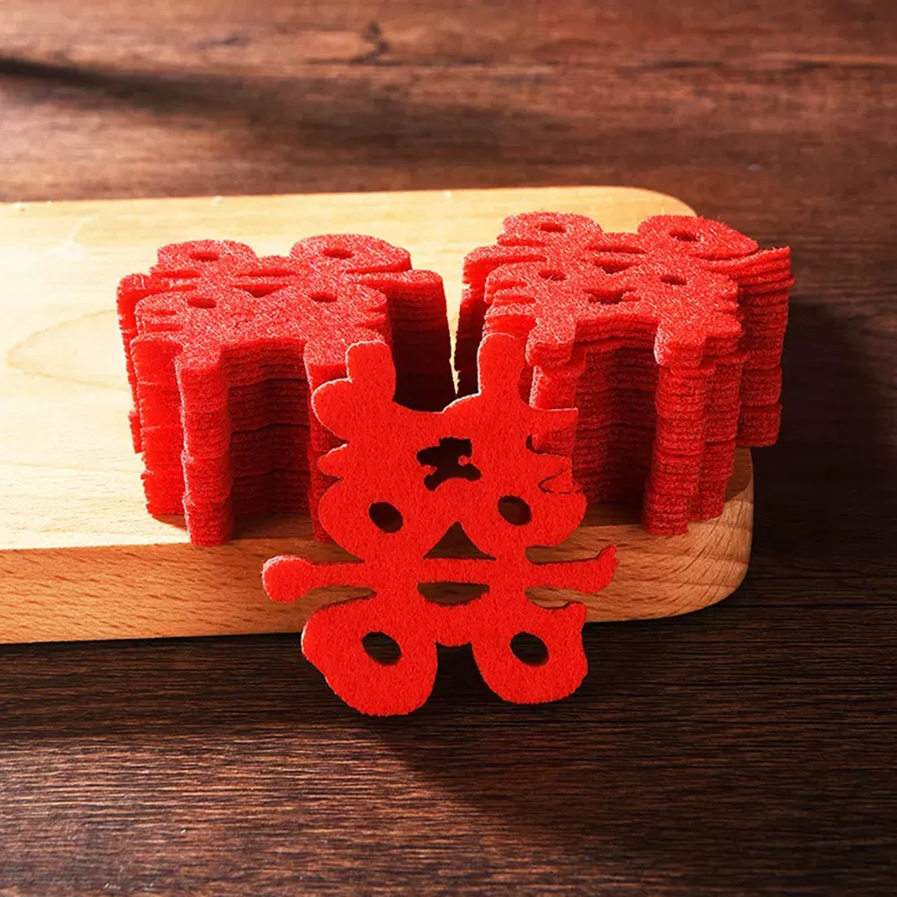 May include: A stack of red felt double happiness symbols, a traditional Chinese wedding symbol, on a wooden surface.