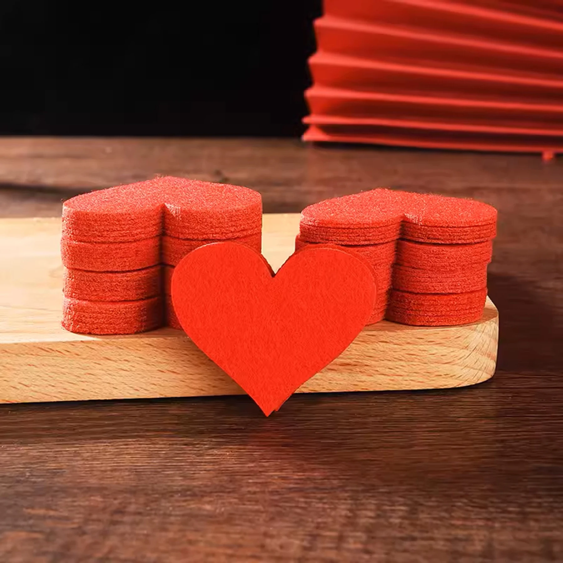 May include: A stack of red felt hearts on a wooden surface. The hearts are arranged in two stacks of seven hearts each, with a single larger heart in front.