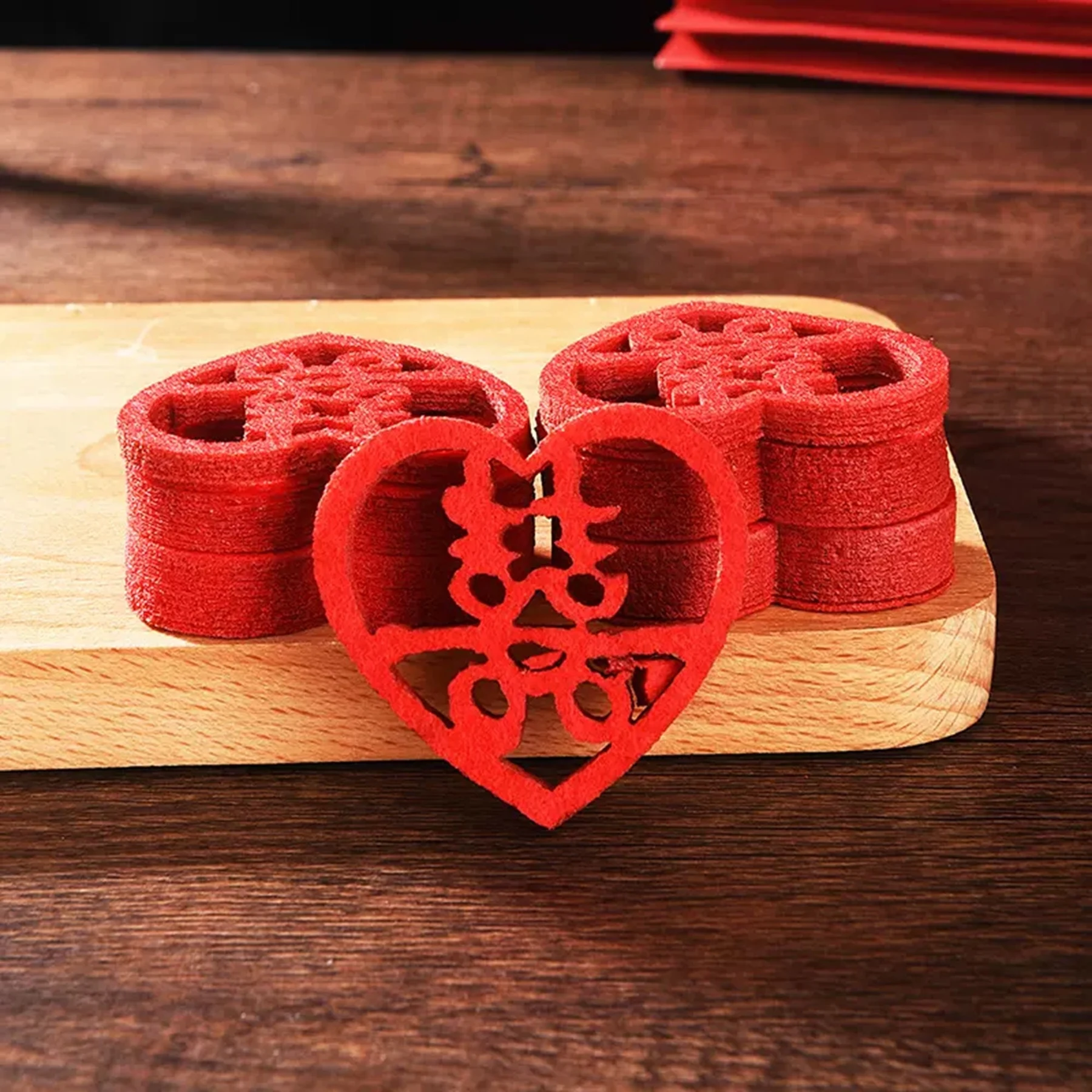 May include: A stack of red felt heart-shaped wedding decorations with a Chinese character for double happiness cut out in the center.