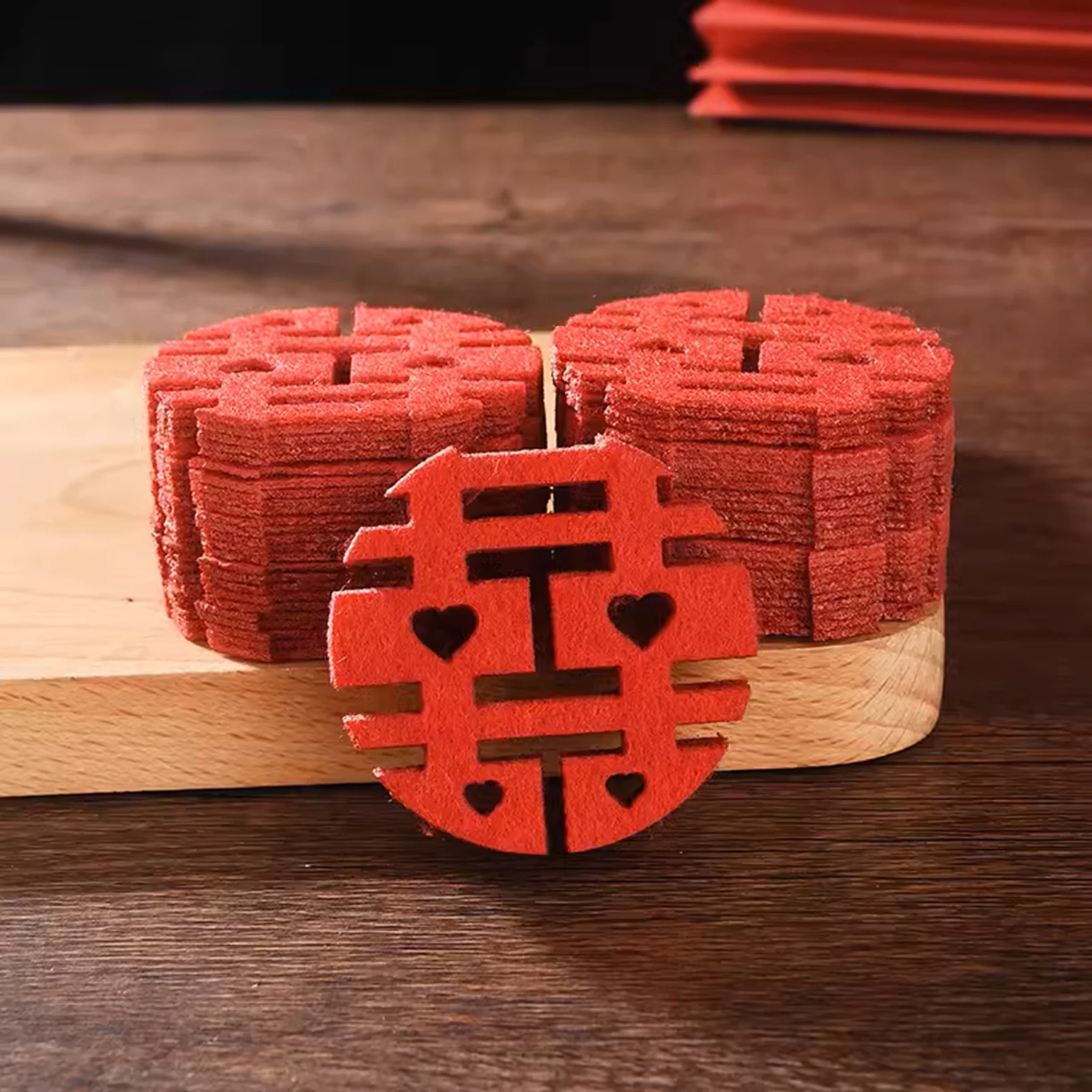 May include: A stack of red felt coasters with a double happiness symbol cut out. The coasters are arranged on a wooden surface.