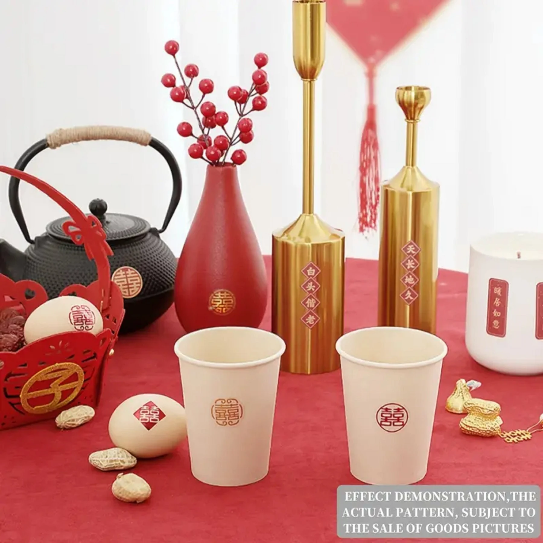 May include: A collection of Chinese wedding decorations on a red tablecloth. Includes a black teapot, red vase with berries, gold candle holders, paper cups, and a red basket with eggs. The cups and eggs have a double happiness symbol.