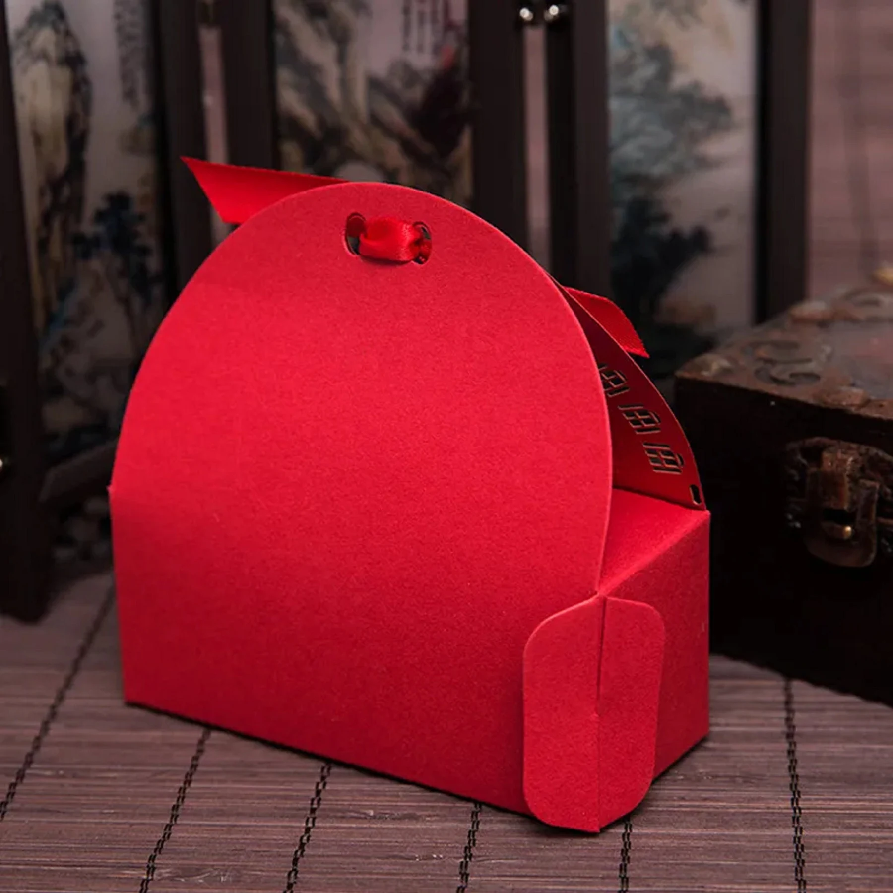 May include: A vibrant red gift box with a curved top and a small red ribbon. The box has a flap closure and a small tag with Chinese characters. The box is made of a textured material.