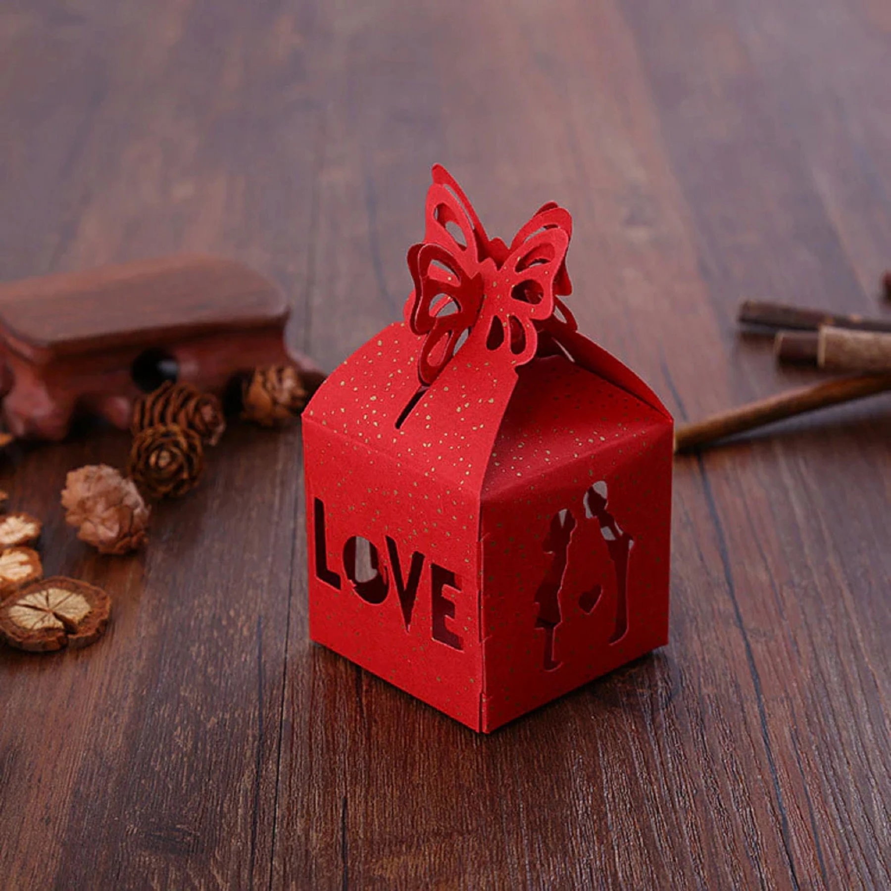 May include: Red paper favor box with a butterfly cutout on the top. The box has a "LOVE" cutout on the front and a silhouette of a couple on the side.