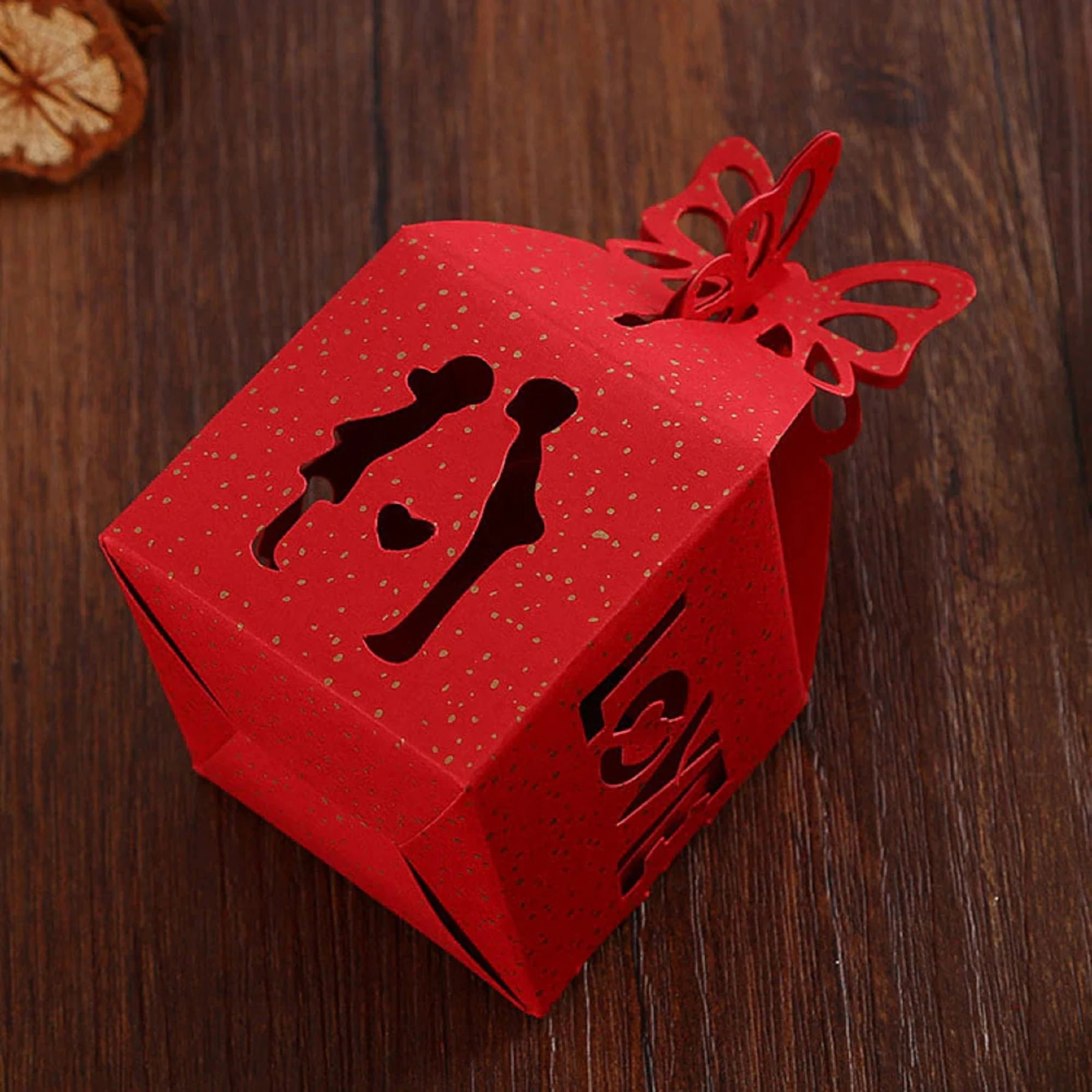 May include: Red paper favor box with a cut-out design of a couple holding hands and a heart. The box has a butterfly-shaped lid and the word "Love" is written on the side.