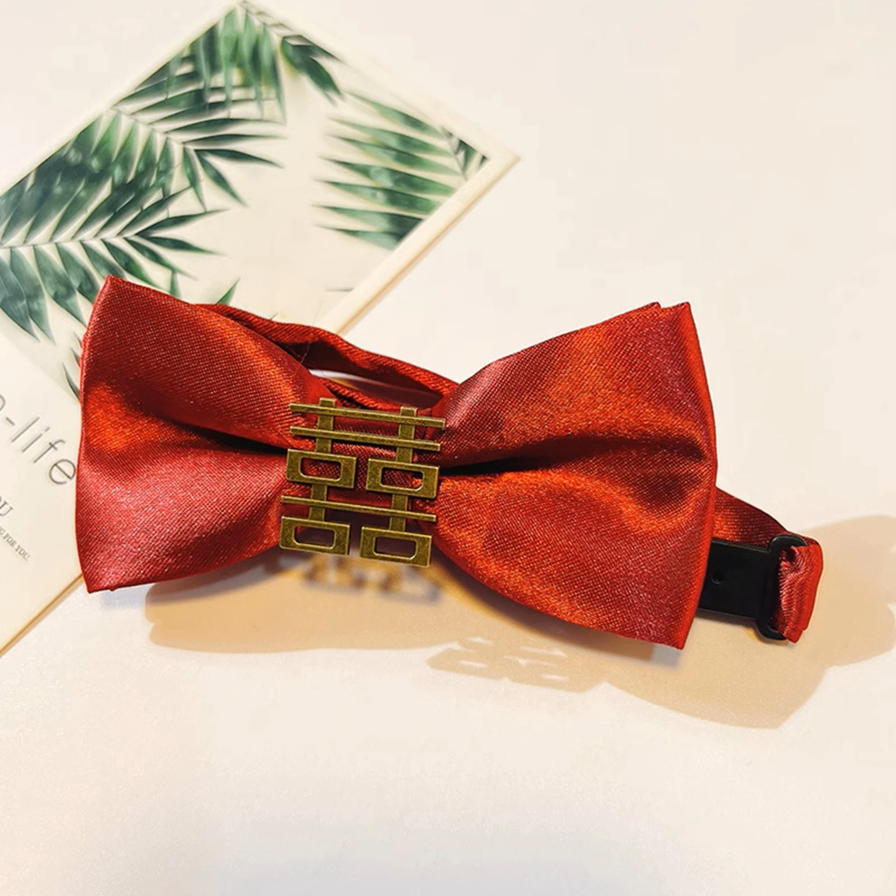 May include: A red bow tie with a gold double happiness symbol charm. The bow tie is made of satin and has a black adjustable strap.