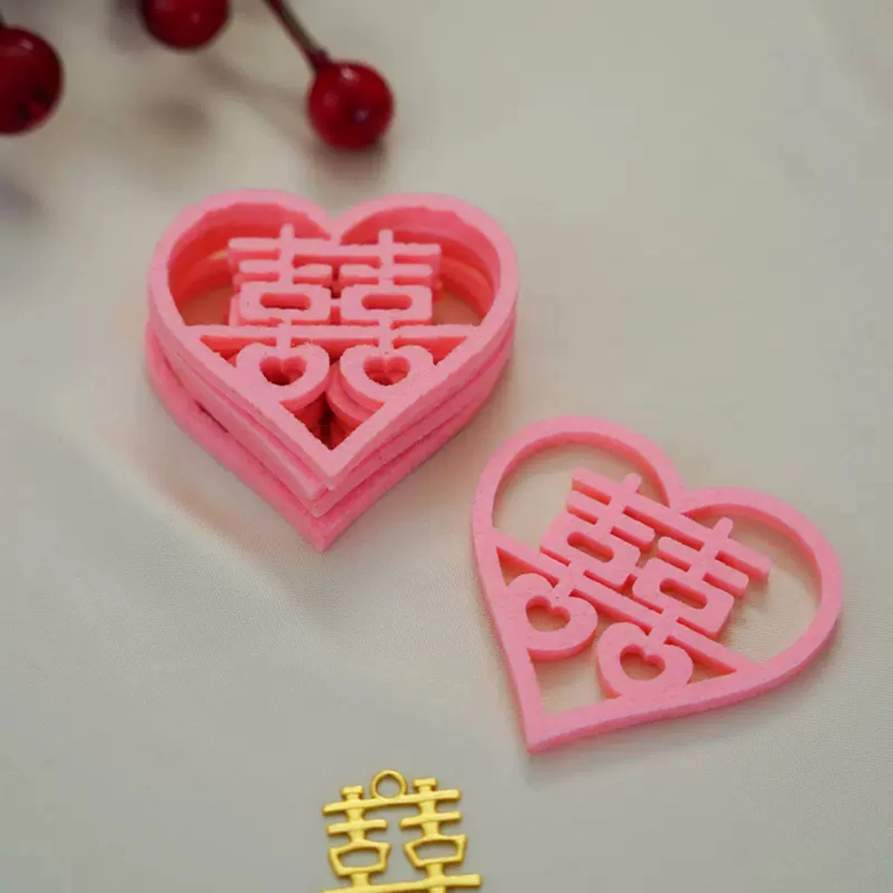 May include: Two pink heart-shaped decorations with the Chinese character for double happiness cut out. The decorations are layered on top of each other. A small gold charm with the same character is also visible.