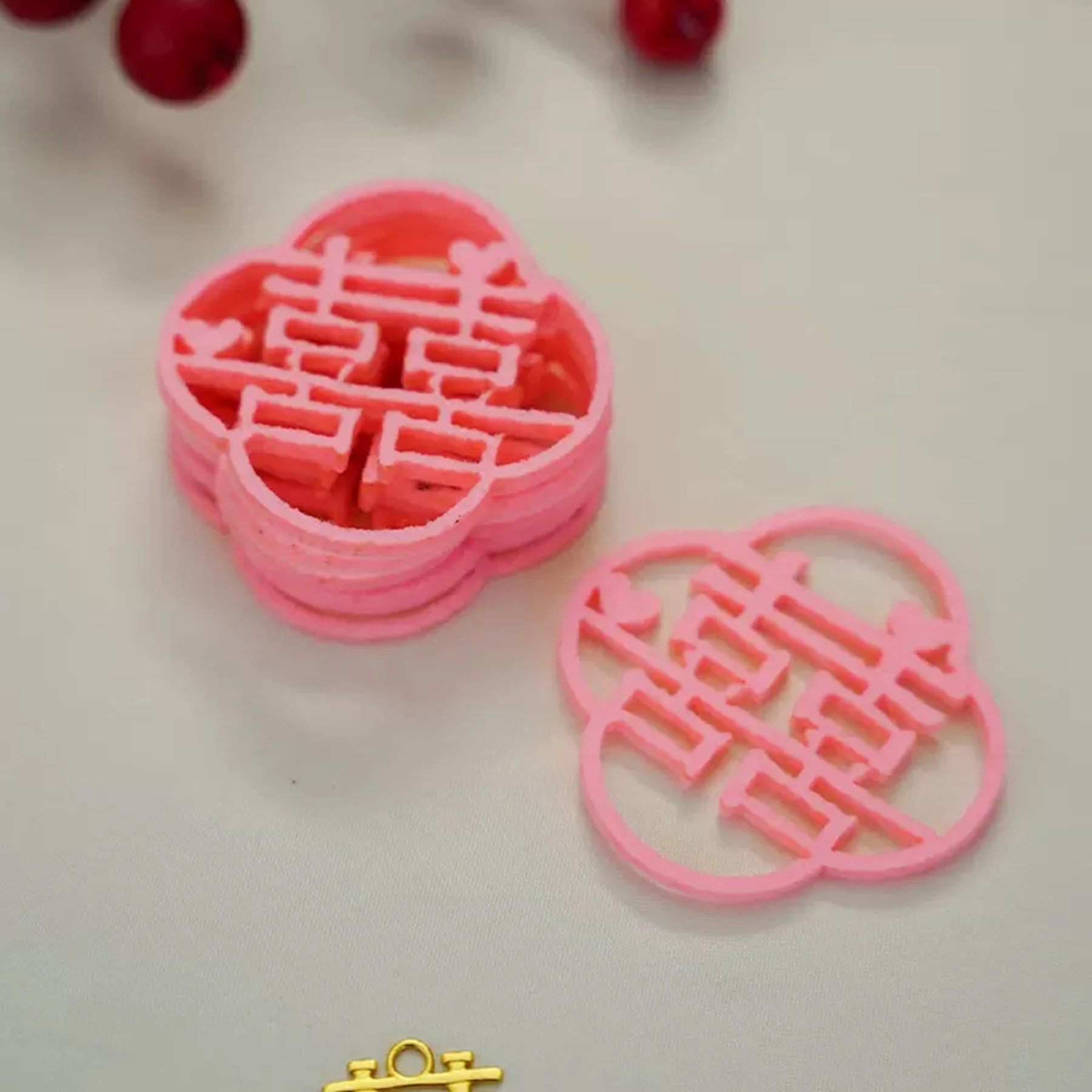 May include: Pink double happiness Chinese character charms, stacked on top of each other. The charms are in the shape of a four-leaf clover. 