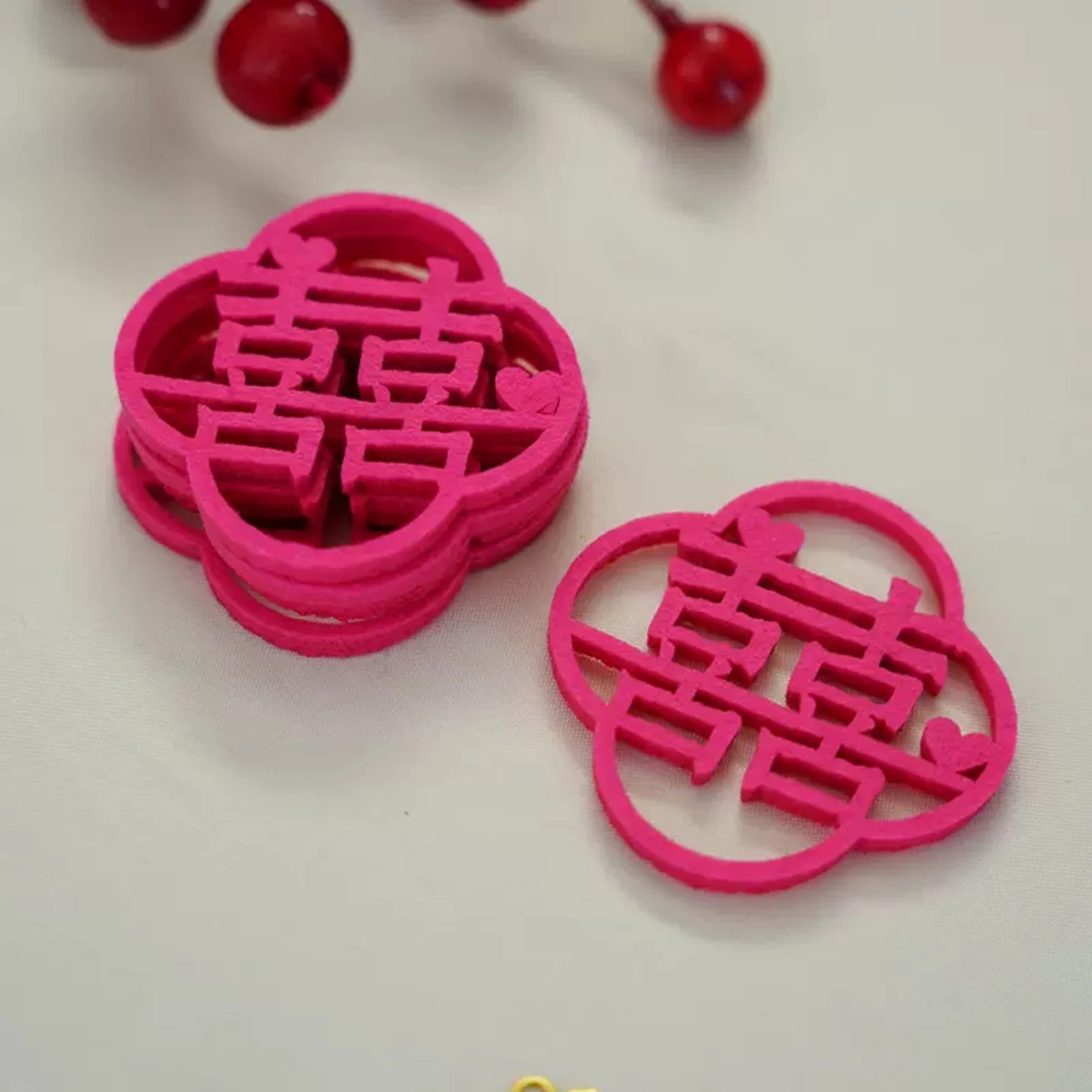 May include: A stack of four pink paper cutouts in the shape of a Chinese double happiness symbol. The symbol is a traditional Chinese character that represents good fortune and happiness in marriage.