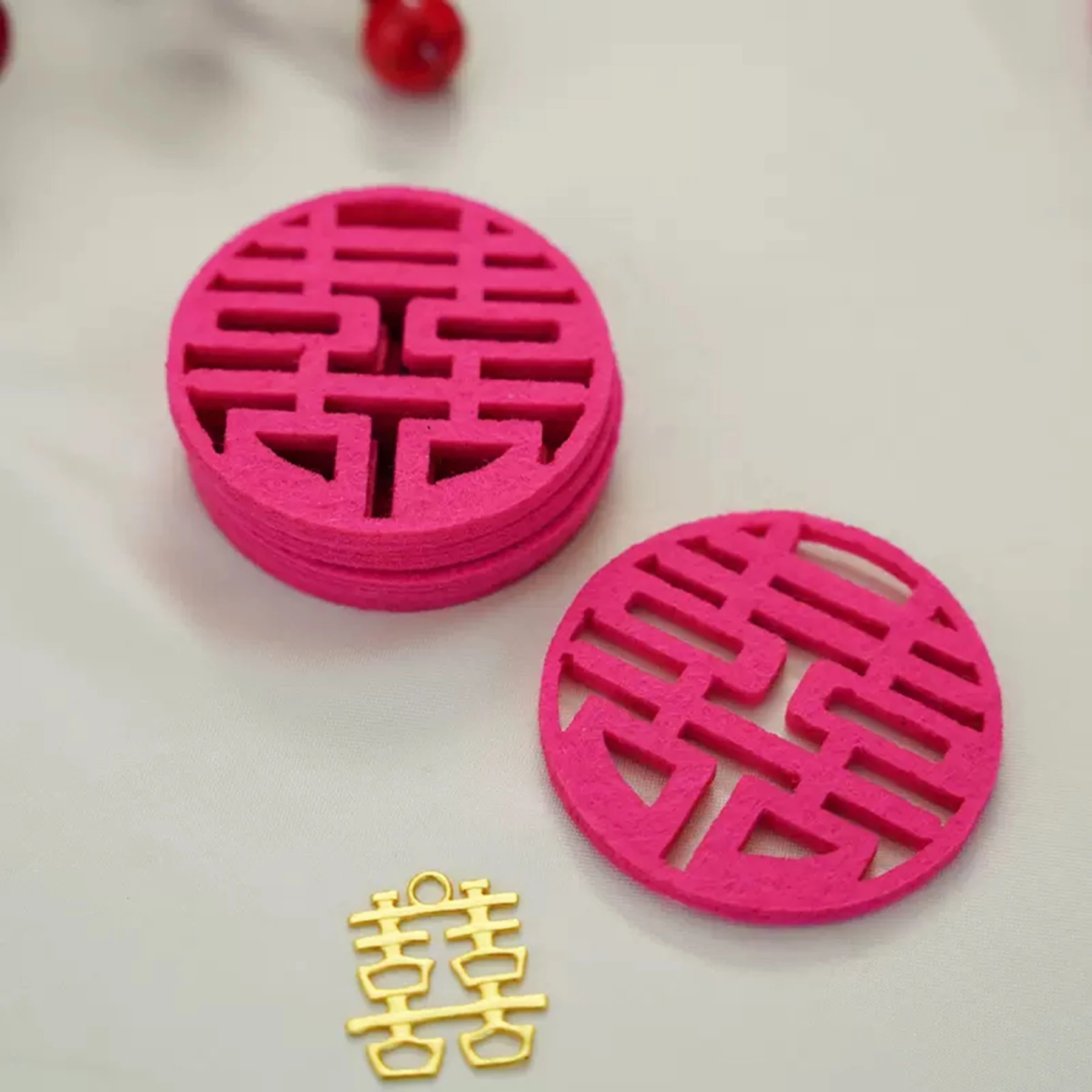 May include: A stack of pink paper cutouts of the Chinese double happiness symbol, with a single gold cutout of the same symbol. The symbol is a traditional Chinese symbol of good fortune and happiness, often used in weddings.